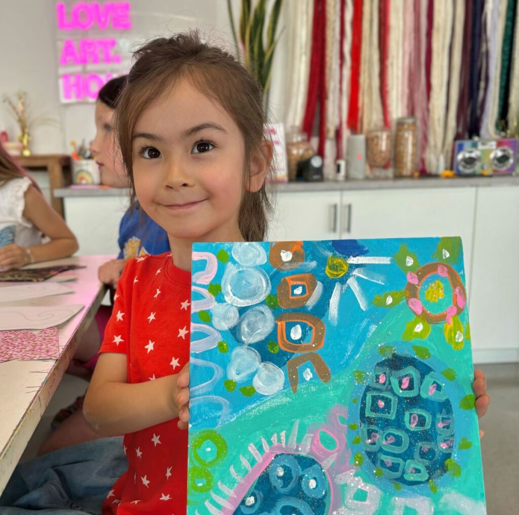 A child smiling and holding a colorful painting