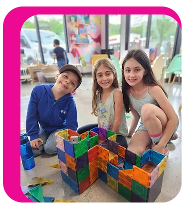 3 children kneeling around a large plastic puzzle builder.