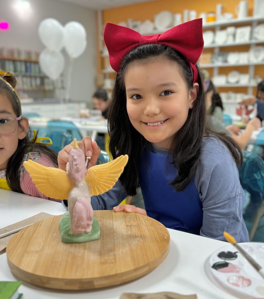 A girl painting a piece of unicorn pottery and smiling